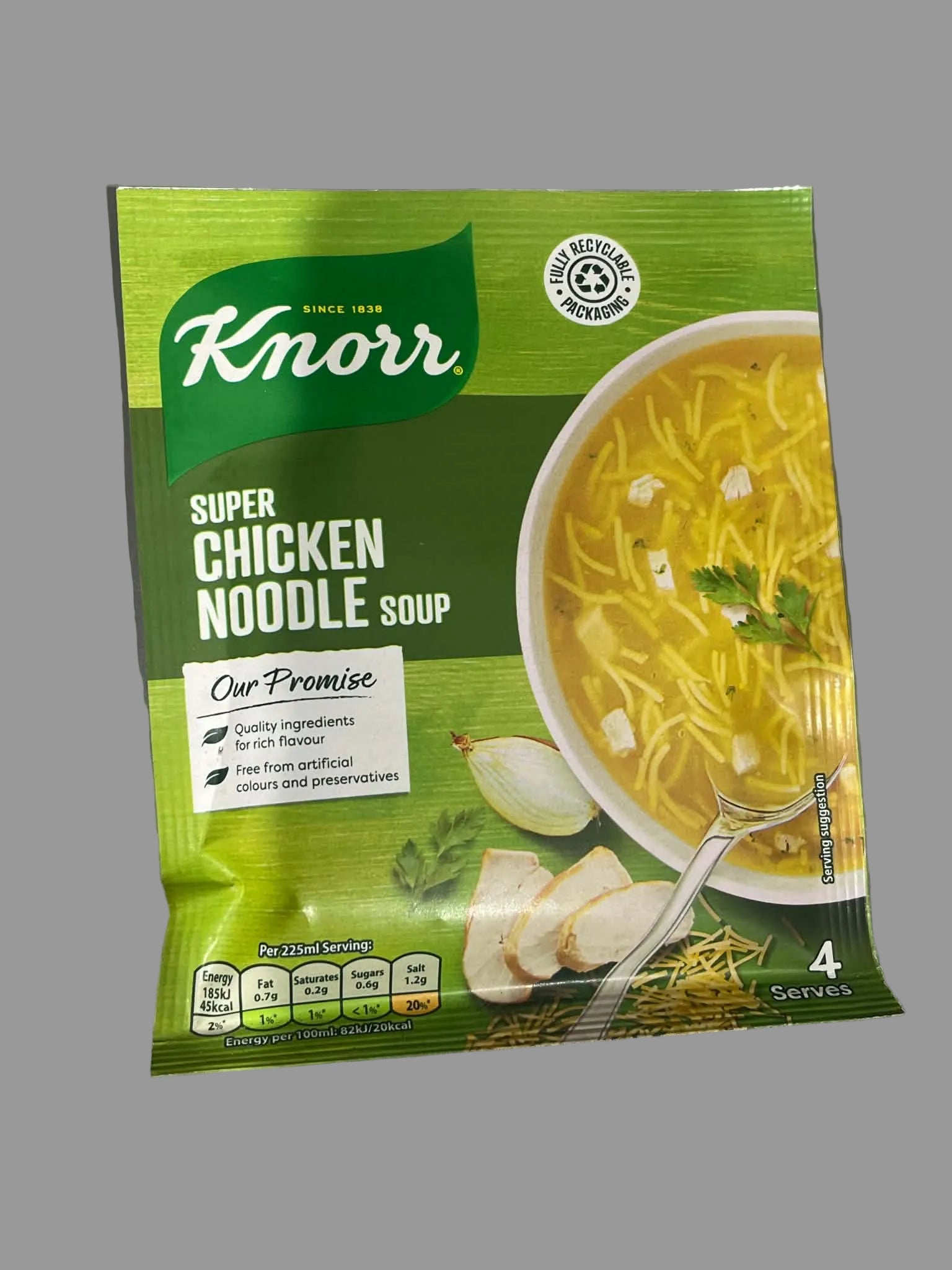A packet of Knorr Super Chicken Noodle Soup on a gray surface. The green packaging features a bowl of yellow noodle soup, sliced chicken, and herbs.
