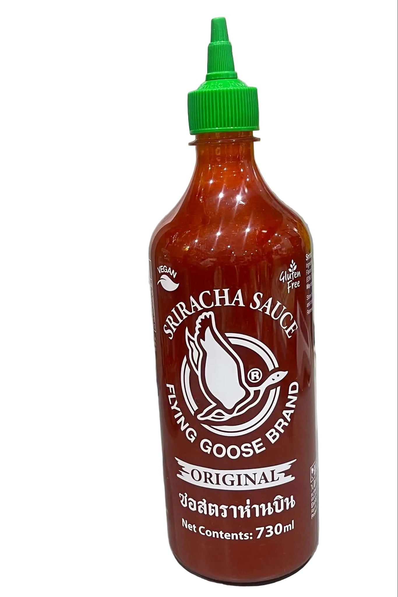A 730ml squeeze bottle of Flying Goose Brand Original Sriracha Sauce, featuring a bright red body and a green cap, set on a light gray surface against a marble-patterned wall.
