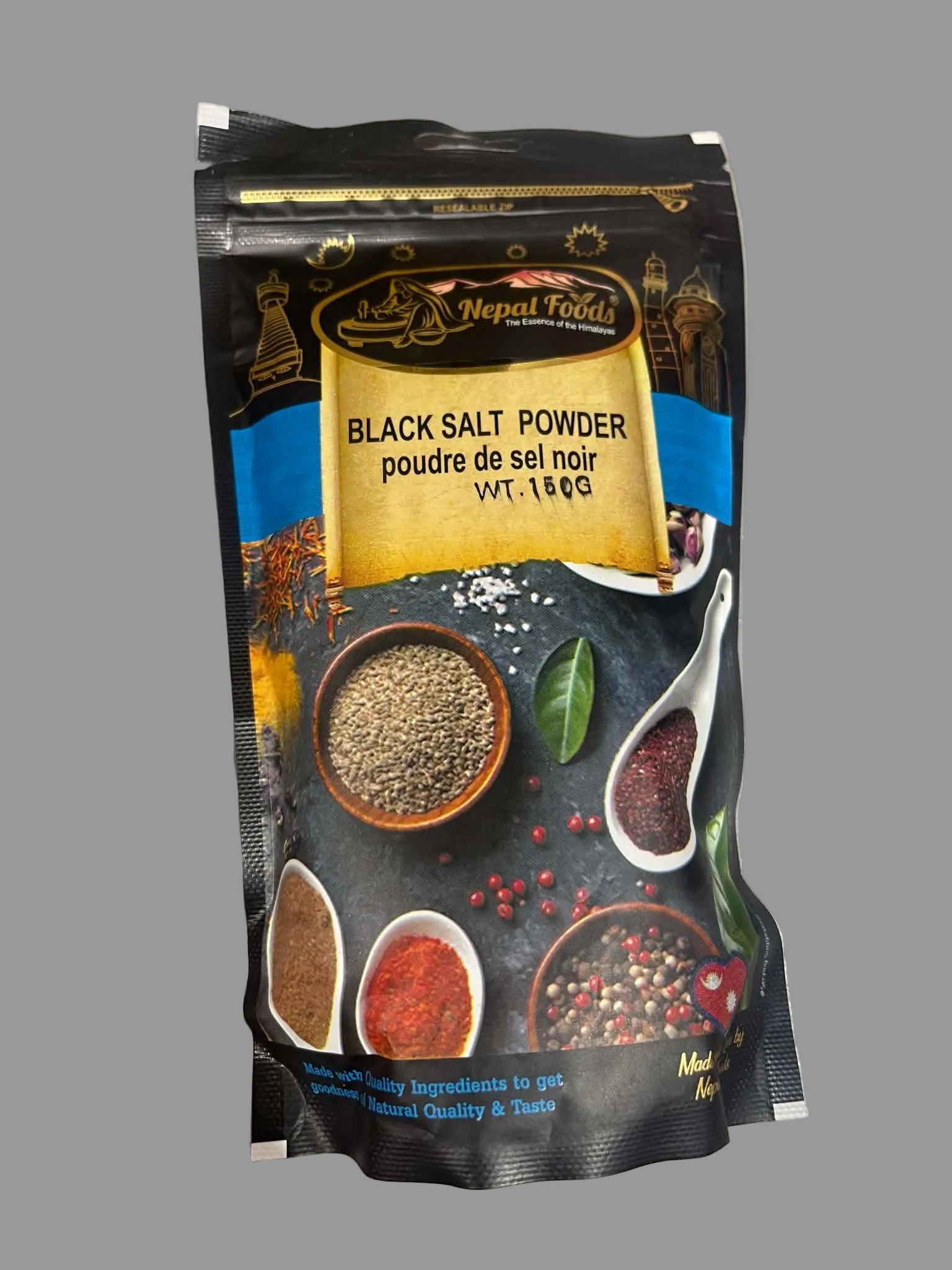 A 150g bag of Nepal Foods Black Salt Powder (poudre de sel noir) on a light gray surface. The packaging is black with a gold label, blue accents, and illustrations of spices and herbs.