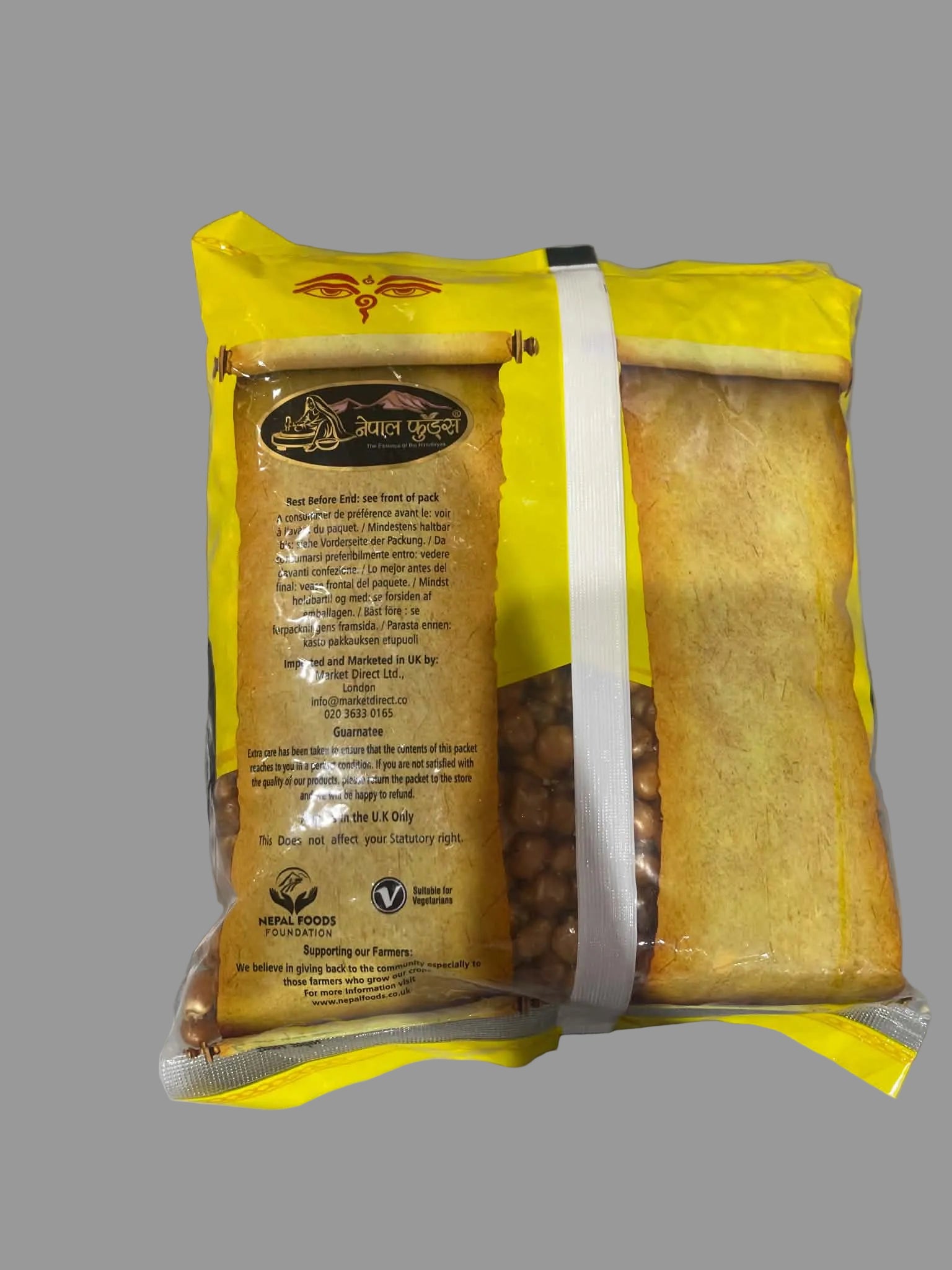 A yellow bag of lentil chips with a white vertical stripe, showing the back of the packaging with text and a clear window revealing the brown lentil chips inside, set on a gray surface.