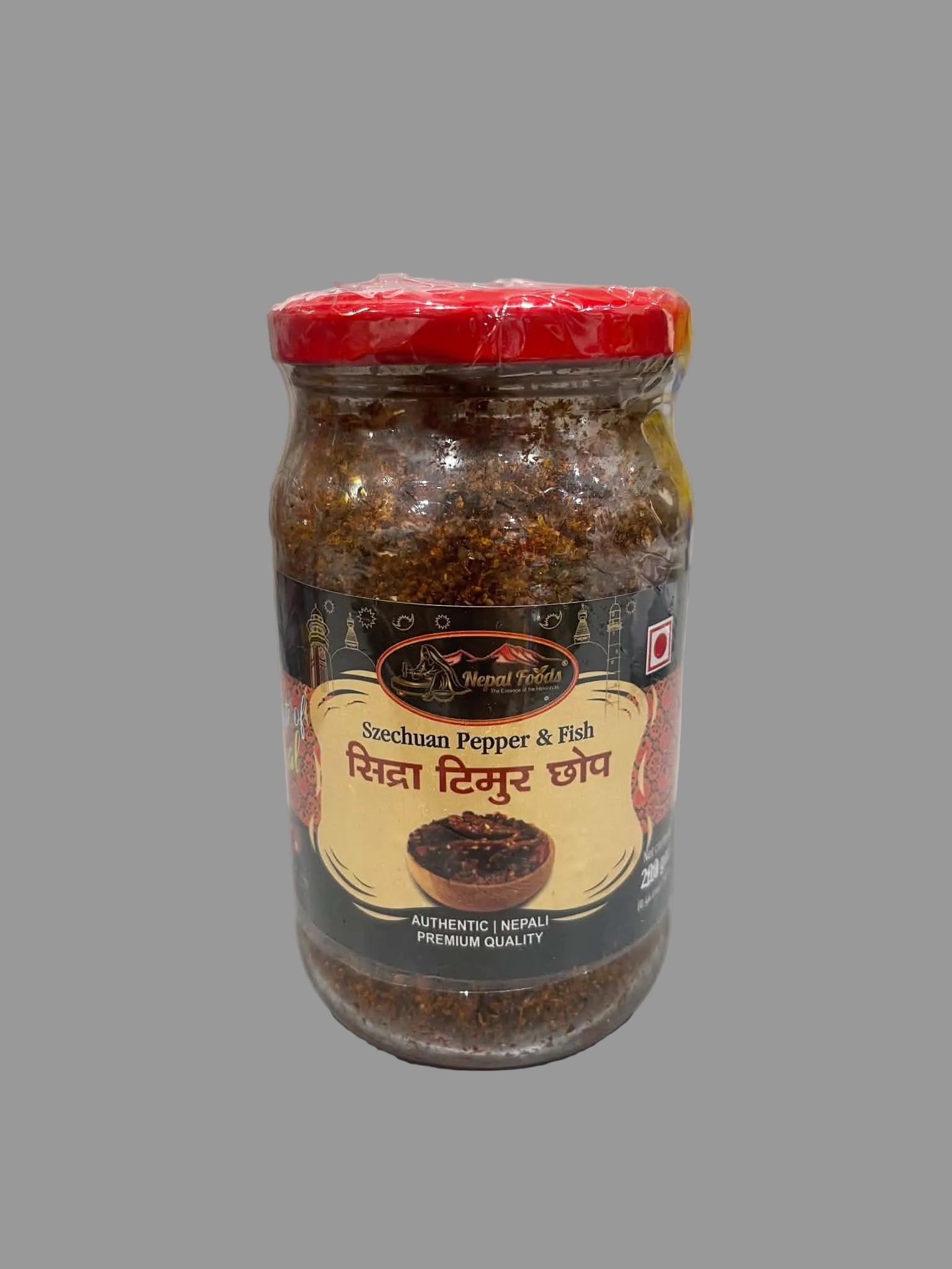 A glass jar of Saechuan Pepper & Fish chutney by Brand Naya, featuring a red lid and a black and gold label with Hindi text, set on a gray surface.