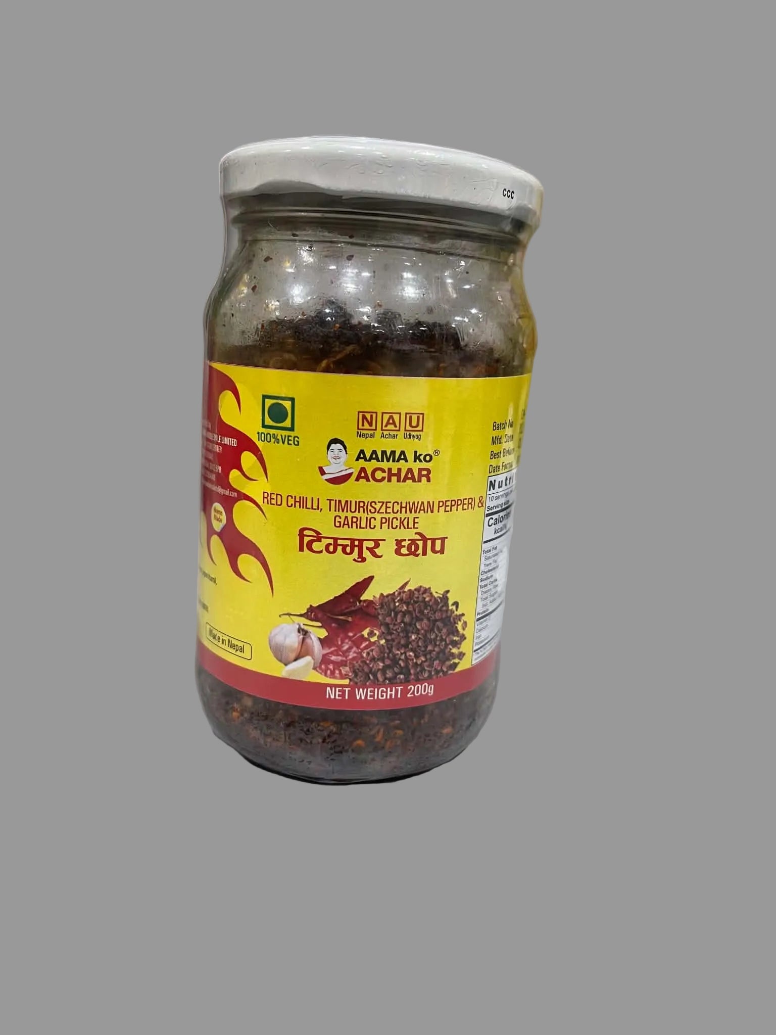 A glass jar of Nau Achar Aama ko Red Chilli Tamrishtwa Garlic Pickle on a light gray countertop with a marble backsplash in the background.