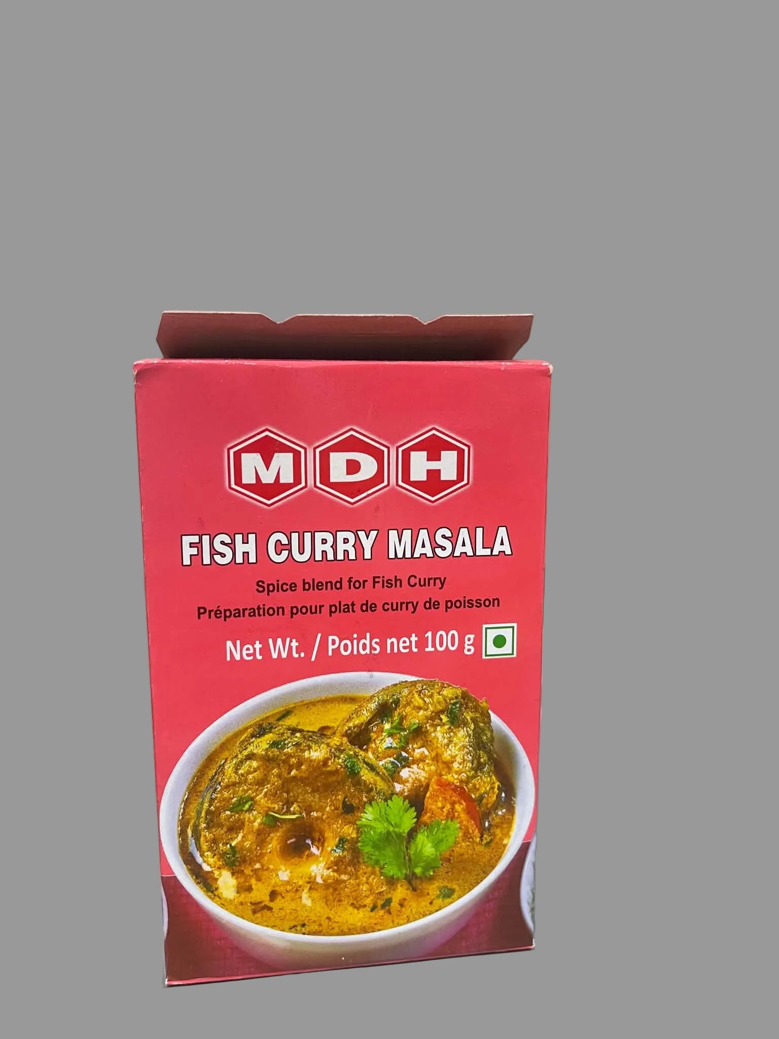A red box of MDH Fish Curry Masala spice blend standing on a gray surface, with a bowl of curry pictured on the front. The background shows a marble-patterned wall and other packaged food items.