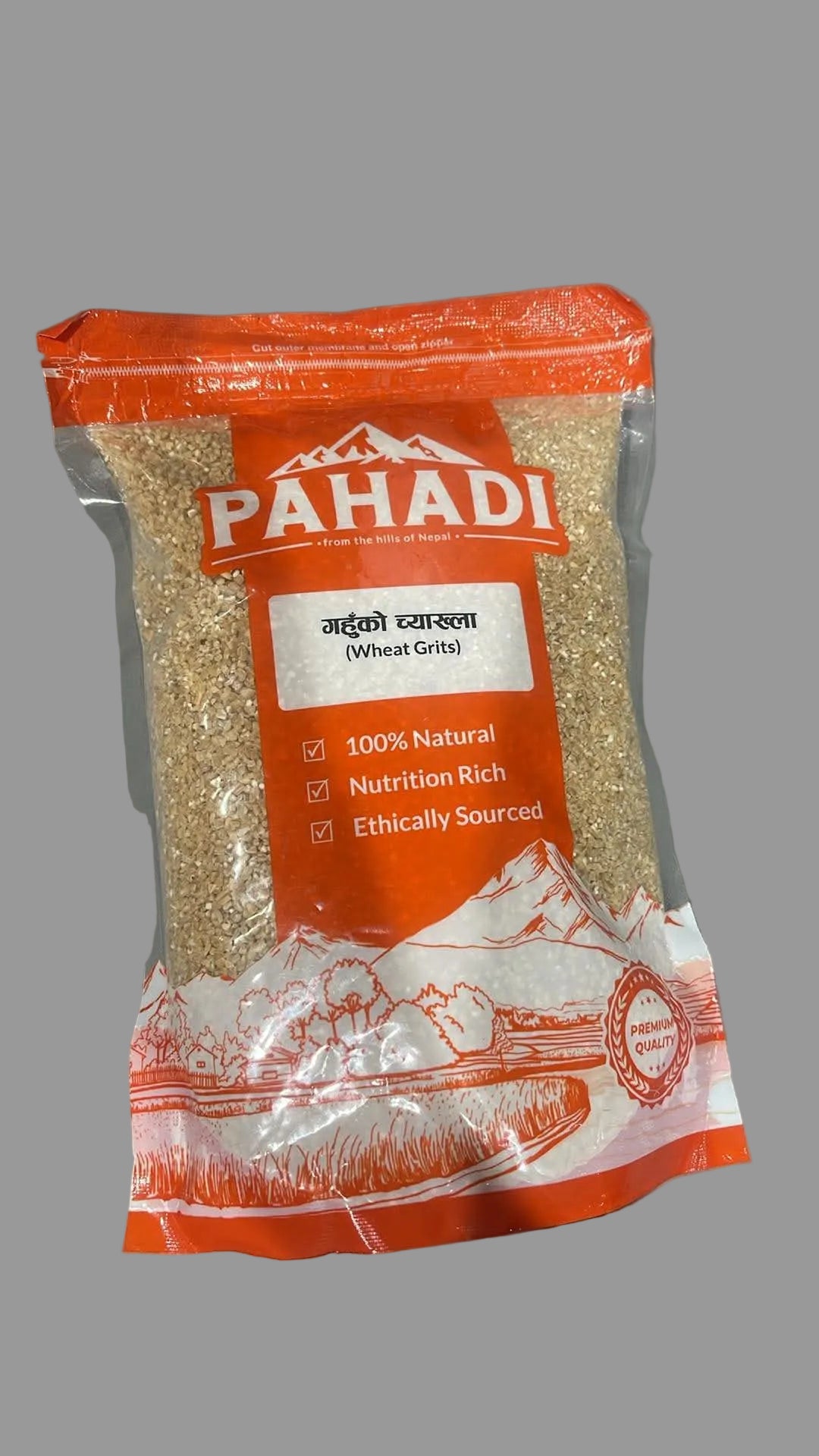 A bag of Pahadi Brand Wheat Grains (Badko Prashana) with orange and white packaging, showing the beige grains inside, placed on a gray surface.