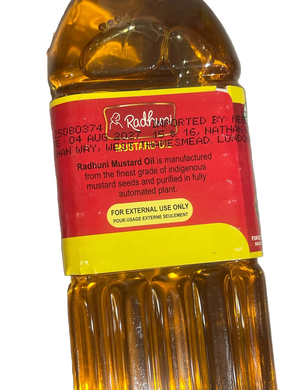 A bottle of Radhuni Mustard Oil with a red and yellow label, photographed against a neutral gray background.