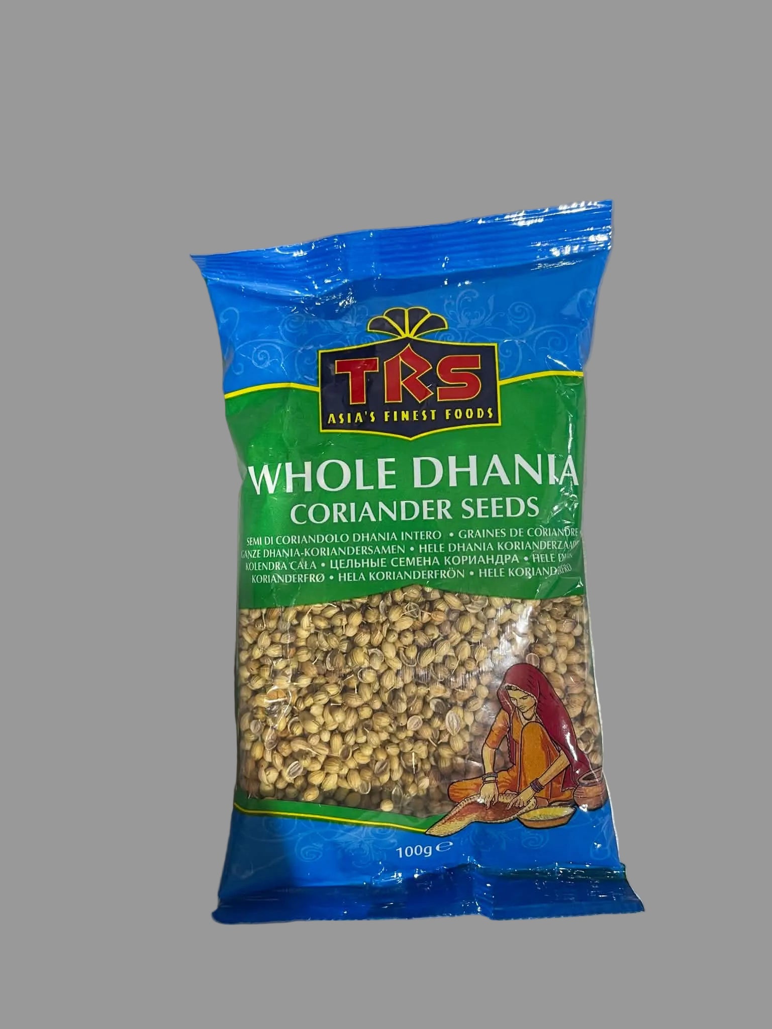 A 100g bag of TRS Whole Dhania Coriander Seeds on a light gray surface. The packaging is blue and green with a clear window showing the whole seeds inside.