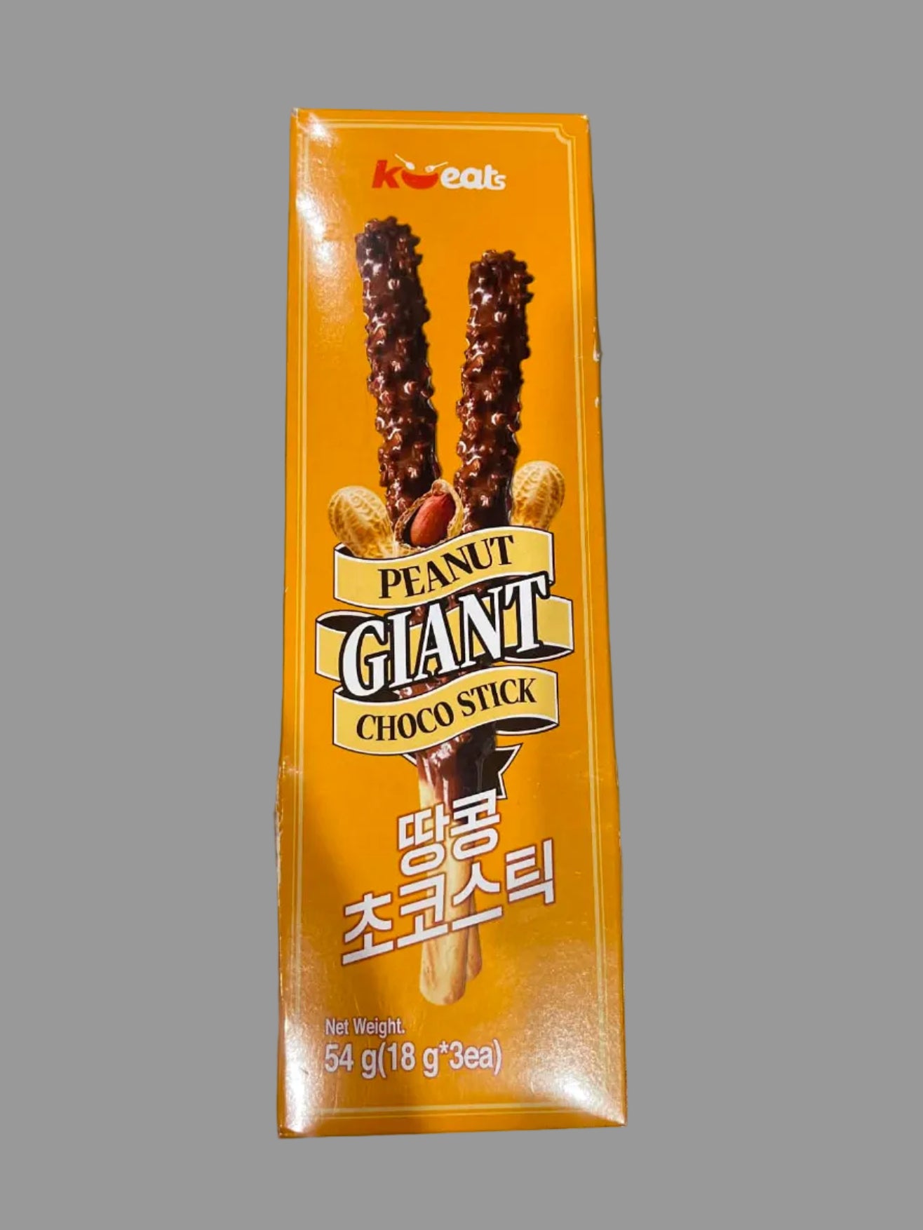 A box of Koreast Peanut Giant Choco Stick snack, featuring an orange package with illustrations of chocolate-covered peanuts and Korean text, placed on a gray surface.