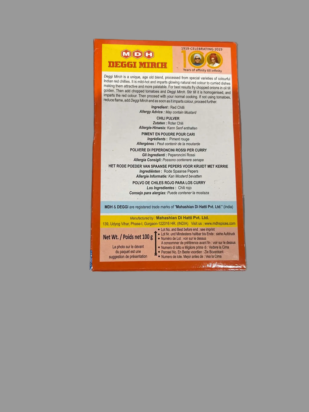 The back of an NDB (Netherlands Dairy Products) Reggi Mirch 100g package, showing ingredients and nutritional information in white text on a bright orange and yellow background, photographed on a gray surface.