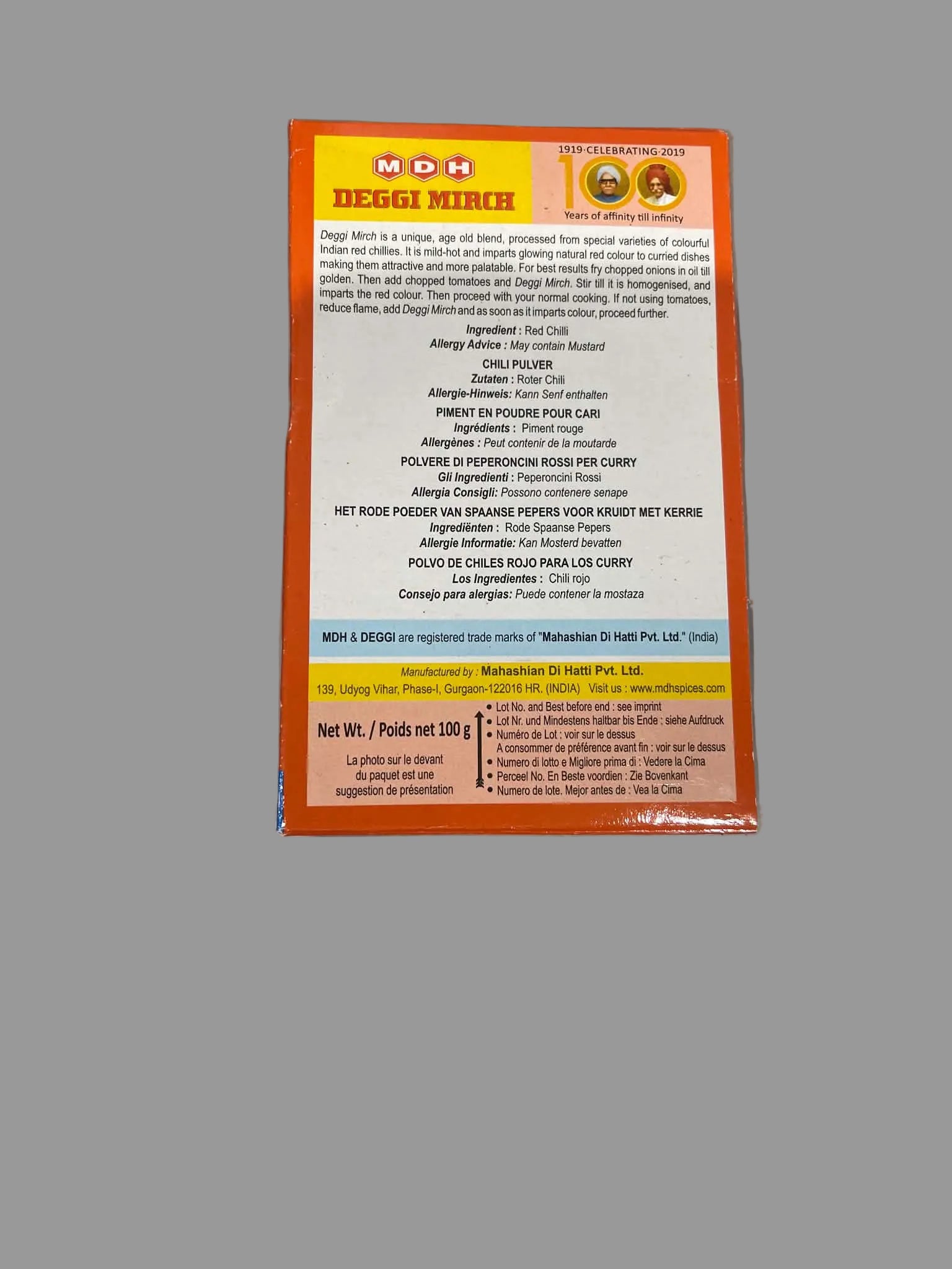 The back of an NDB (Netherlands Dairy Products) Reggi Mirch 100g package, showing ingredients and nutritional information in white text on a bright orange and yellow background, photographed on a gray surface.
