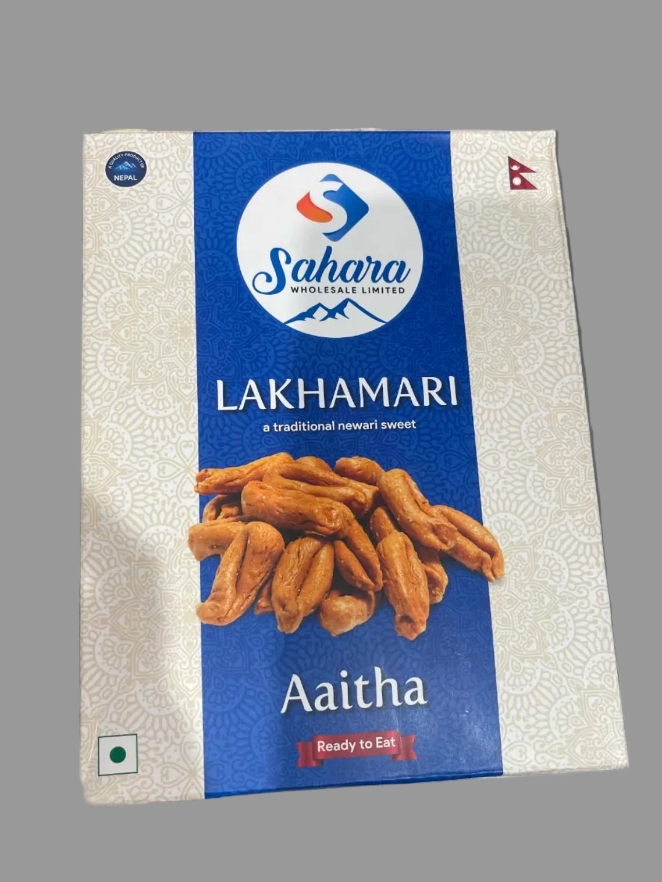 A box of Sahara Wholesale Limited Lakhamari Aaitha ready-to-eat sweets, featuring a blue and white design with an image of golden-brown fried sweets on the front, photographed on a gray surface.