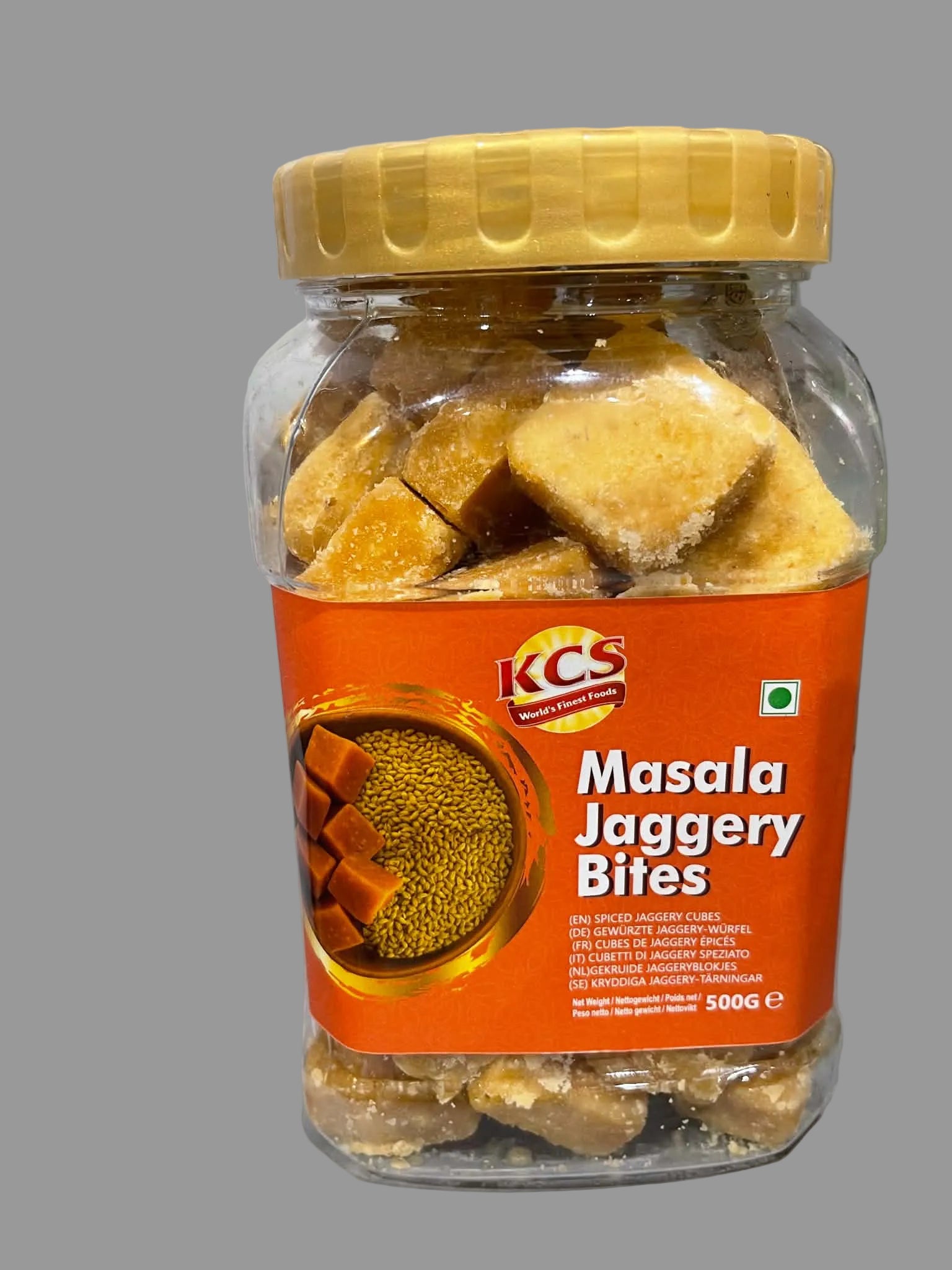 A 500g jar of KCS Masala Jaggery Bites, showing the golden-brown sugar cubes inside a clear plastic container with a bright orange label and a yellow lid.
