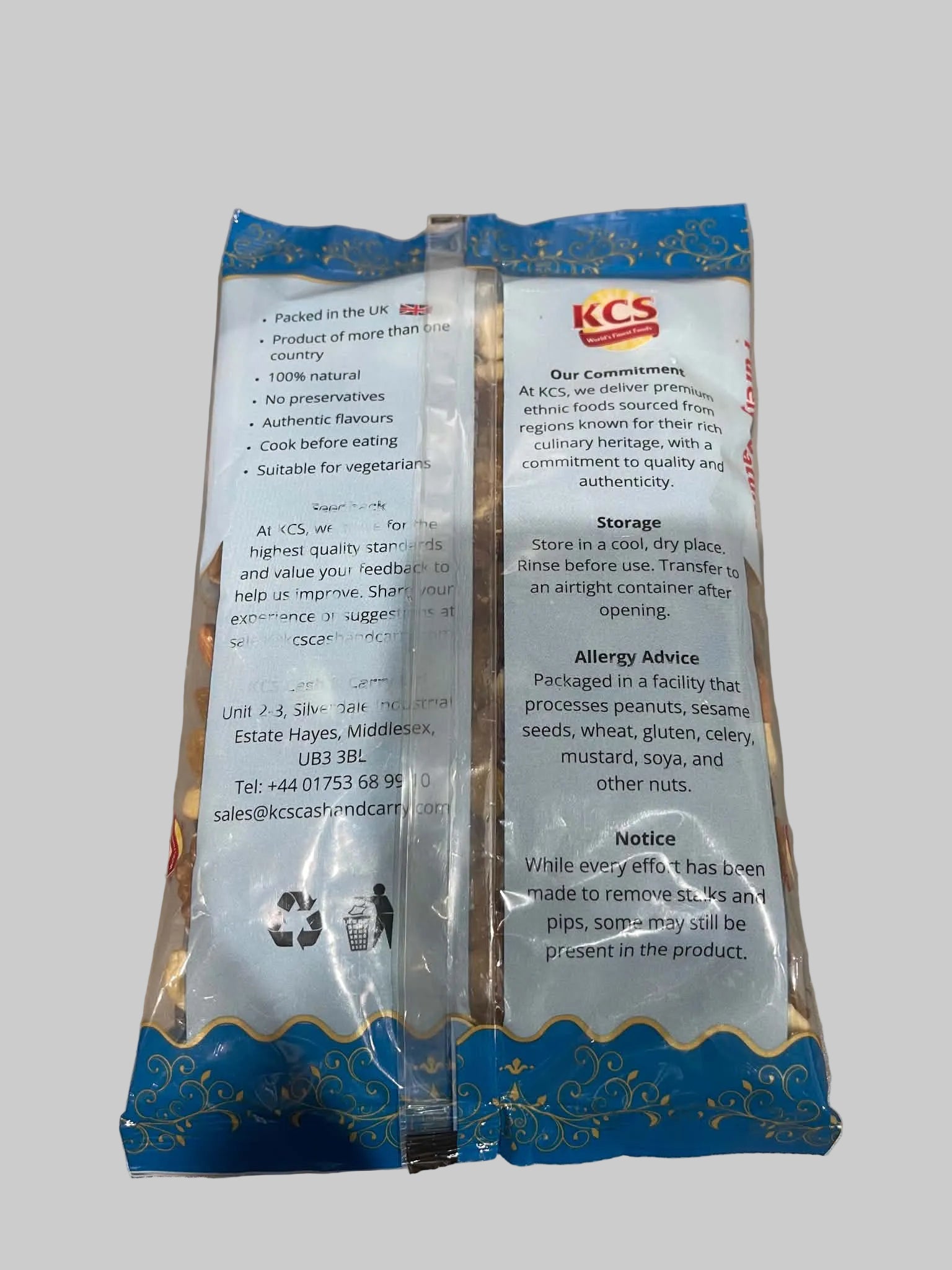 Two sealed KCS brand food packets standing upright on a light countertop, showing the back side with printed instructions, storage, and allergy information. The packets are mostly white with blue decorative borders and a red KCS logo.