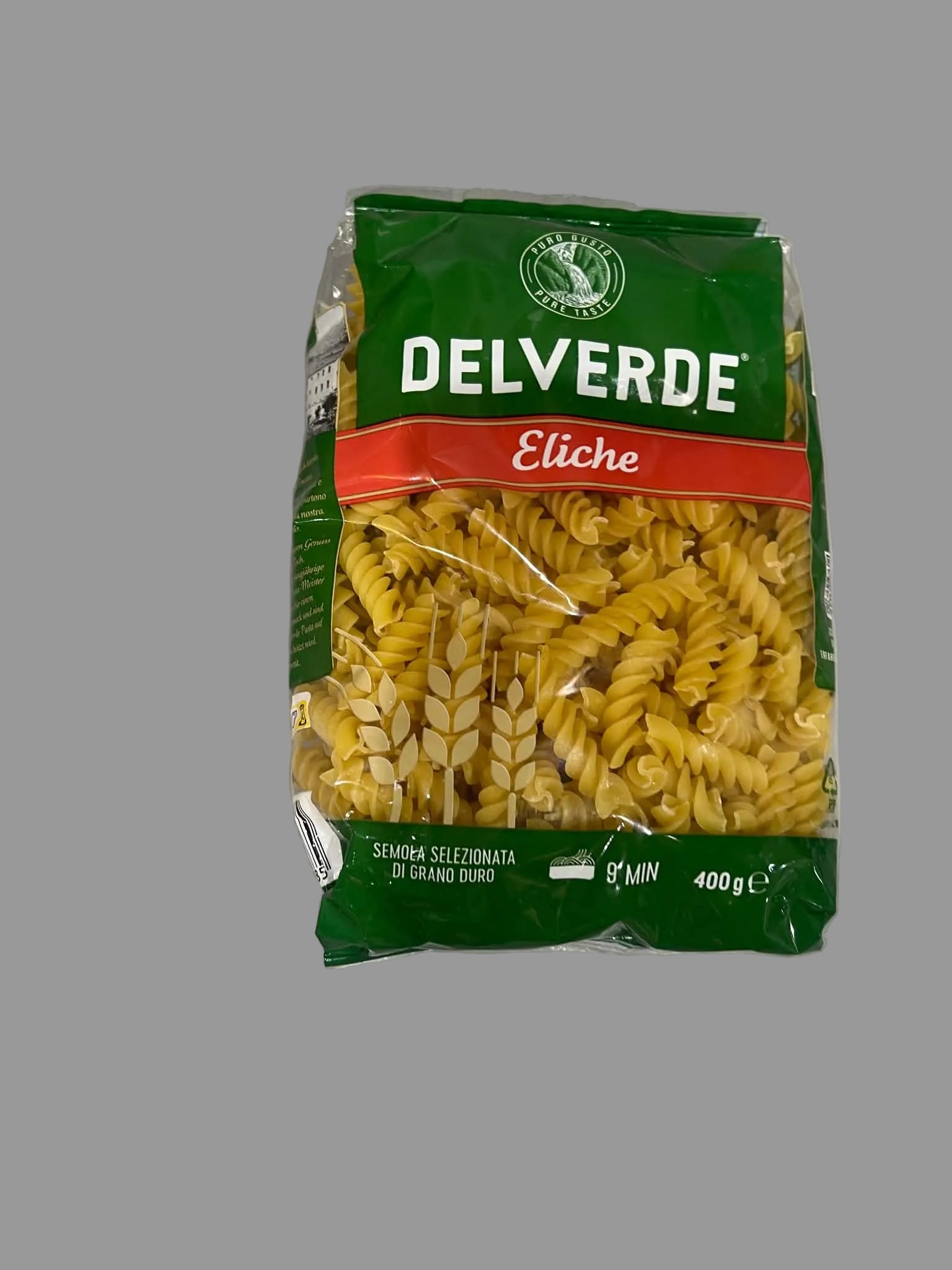 A 400g bag of Delverde Eliche semolina rotini pasta, showing the green and red packaging with a clear window displaying the yellow pasta inside, set on a gray surface.