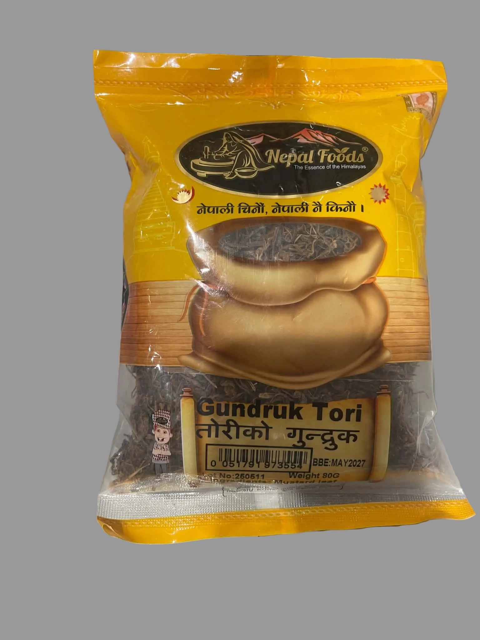 A bag of Nepal Foods Gundruk Tori (dried tea) on a gray surface. The packaging is primarily yellow with a graphic of a golden teapot and shows the brand 'Nepal Foods' in a black oval logo at the top.