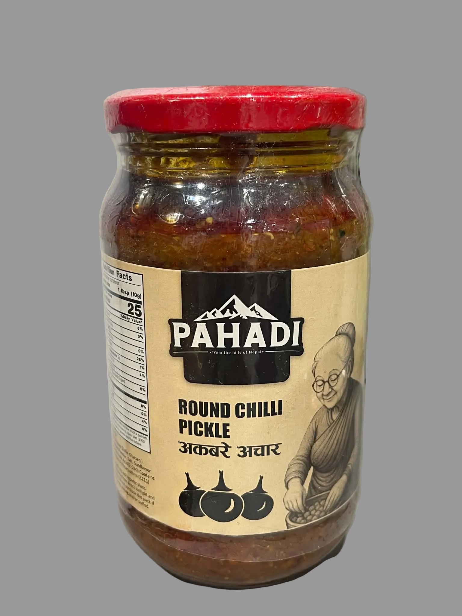 A jar of Pahadi Round Chilli Pickle with a red lid and beige label, photographed on a light countertop with a blurred kitchen background.