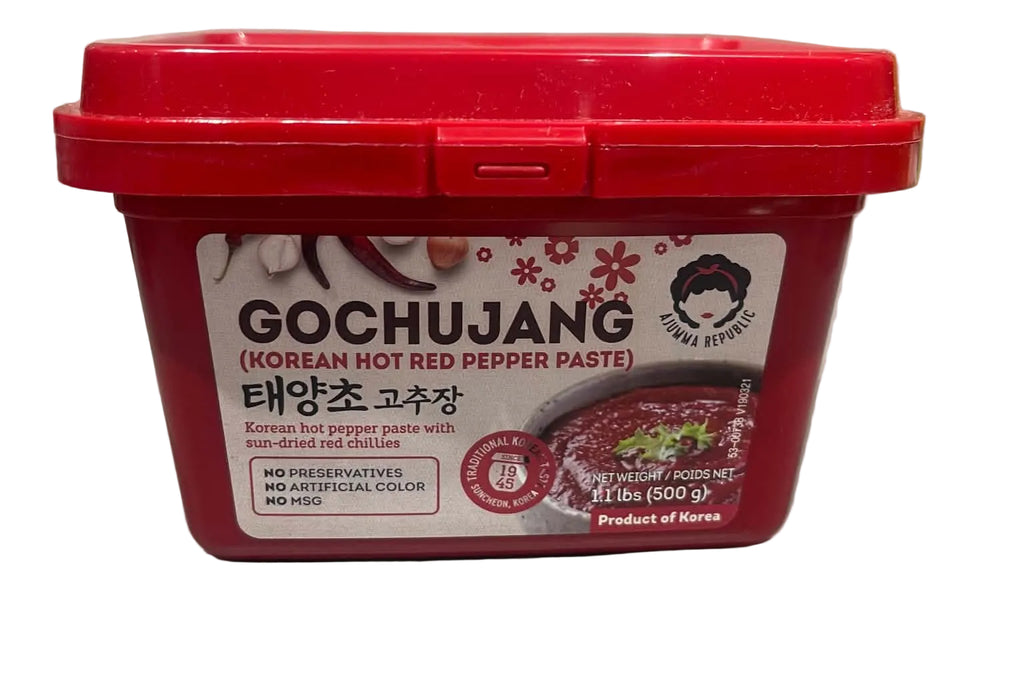A red plastic tub of Gochujang Korean hot red pepper paste on a light gray countertop with a marble backsplash in the background.