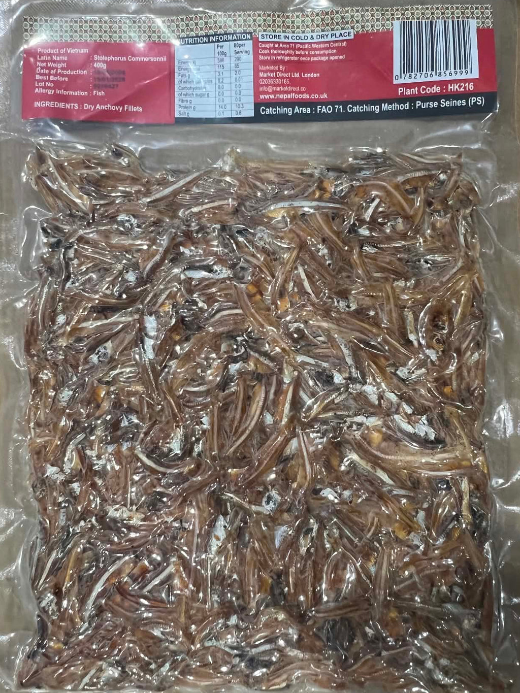 A vacuum-sealed plastic bag filled with dried small fish, photographed from above on a brown cardboard surface. The package has a red and black label with a barcode on the right side.