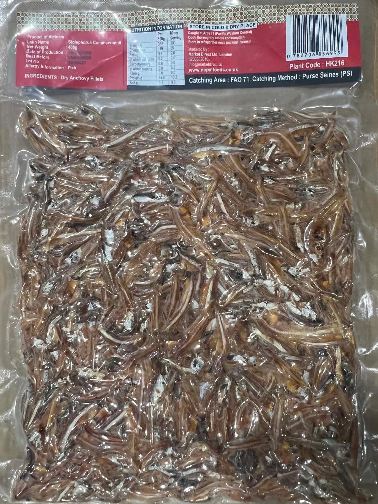 A vacuum-sealed plastic bag filled with dried small fish, photographed from above on a brown cardboard surface. The package has a red and black label with a barcode on the right side.
